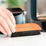Hand using a wooden brush to sweep coffee grounds off a worktop.