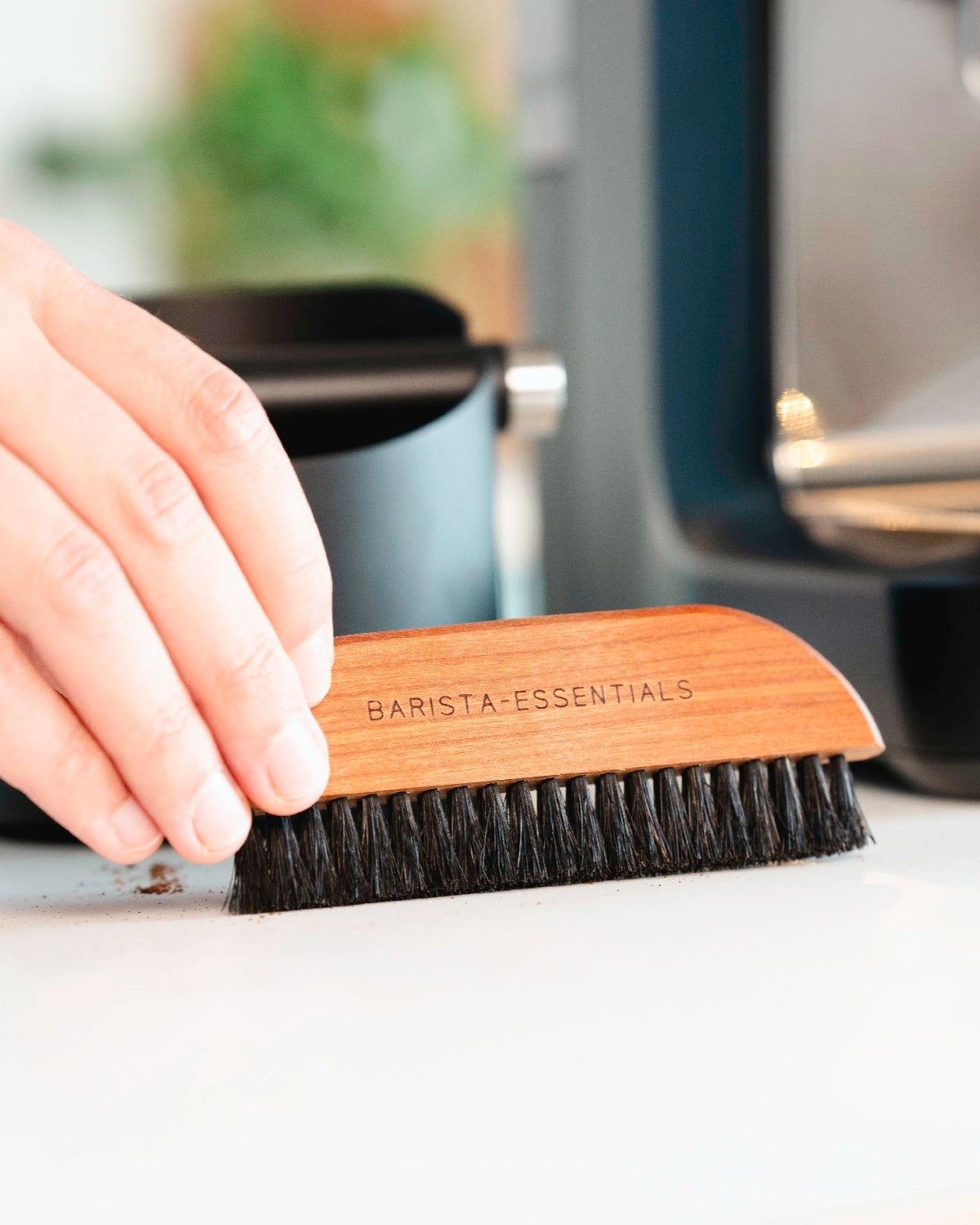 Hand using a wooden brush to sweep coffee grounds off a worktop.